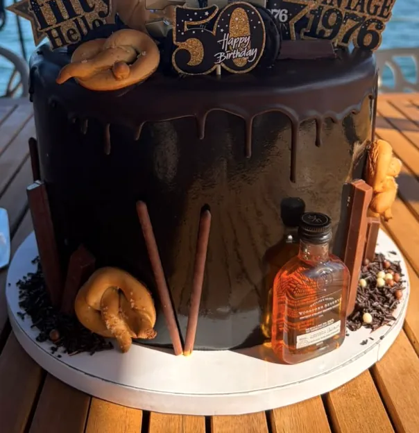 Bolo de chocolate com cobertura a escorrer, pretzels e toppers dourados de 50 anos