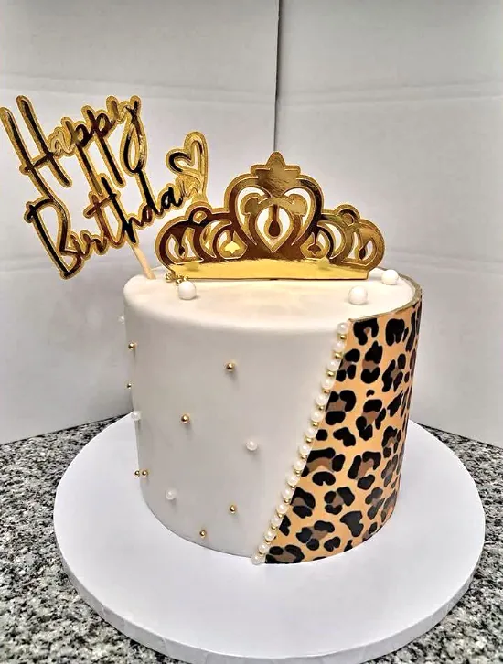 Bolo branco com um lado em padrão de leopardo, pérolas e coroa dourada com Happy Birthday