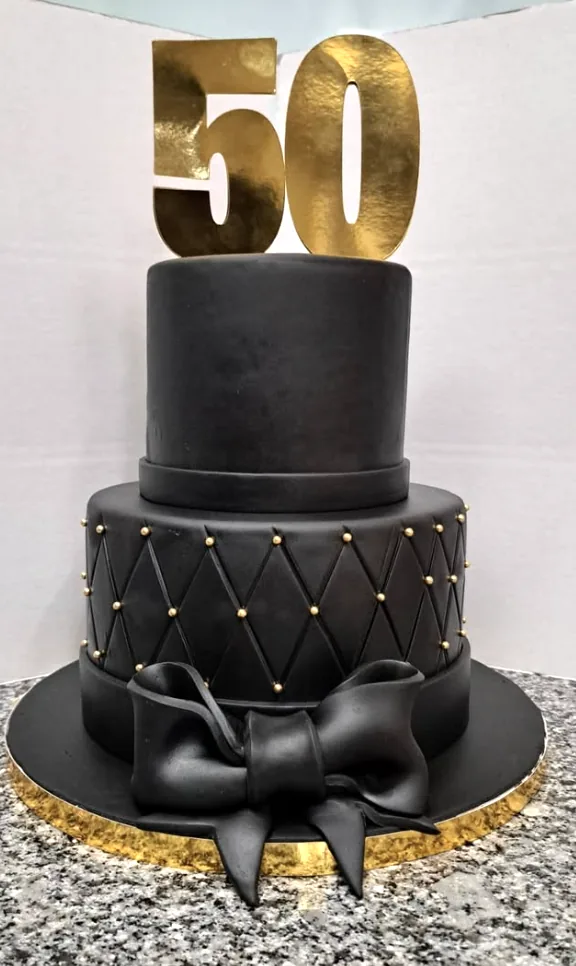 Bolo preto de dois andares com padrão acolchoado, laço e o número 50 dourado